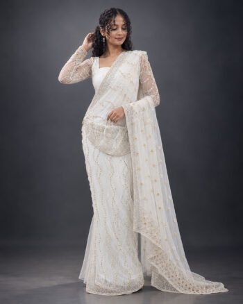 A woman wearing an elegant white and gold bridal saree with intricate embroidery, lace borders, and delicate floral detailing, posing in a studio