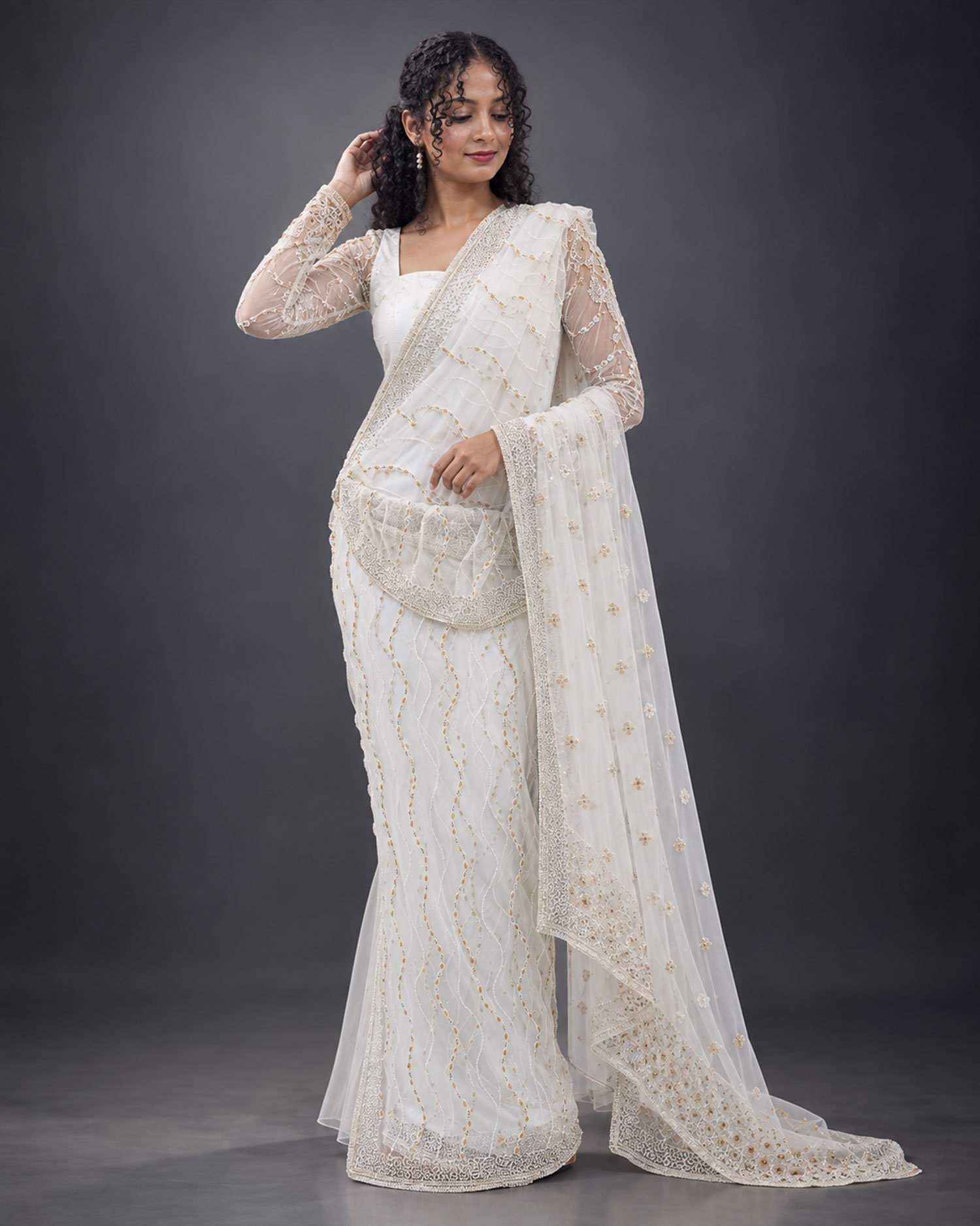 Elegant White & Gold Bridal Saree A woman wearing an elegant white and gold bridal saree with intricate embroidery, lace borders, and delicate floral detailing, posing in a studio