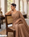 A luxurious champagne-brown embellished fabric with intricate shimmering details, shown styled as a saree