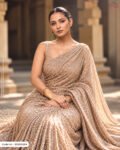 A woman wearing a luxurious champagne-gold embellished fabric styled as an elegant saree, showcasing its dense shimmering texture and intricate sparkling details