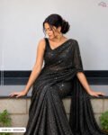 A woman wearing luxurious black shimmering embellished fabric styled as an elegant saree, showcasing its sparkling texture and intricate sequin detailing