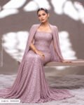 A woman sitting on a wooden bench in a strapless evening gown and matching cape made of mauve/dusty pink sequined fabric