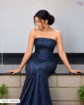 A woman sitting on a ledge wearing a strapless evening gown made of royal navy blue sequined fabric