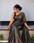 A woman sitting on a ledge draped in an emerald green saree featuring dense copper/bronze foil work, paired with a black sleeveless blouse