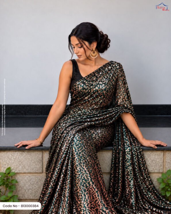 A woman sitting on a ledge draped in an emerald green saree featuring dense copper/bronze foil work, paired with a black sleeveless blouse