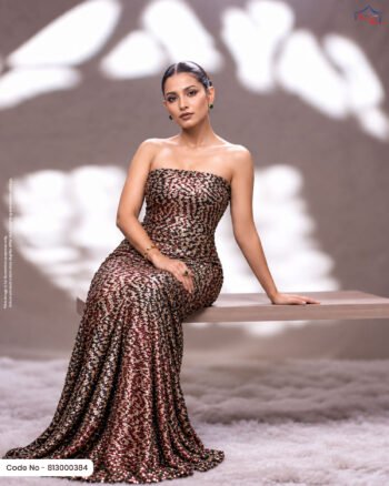 A woman sitting on a wooden bench in a strapless evening gown made of deep maroon and gold foil printed fabric