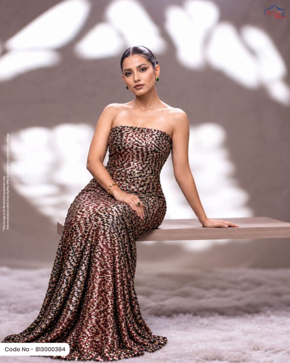 A woman sitting on a wooden bench in a strapless evening gown made of deep maroon and gold foil printed fabric