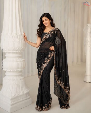 A woman wearing an elegant black saree with intricate gold floral embroidery and a delicate embellished border, posing in a luxurious indoor setting